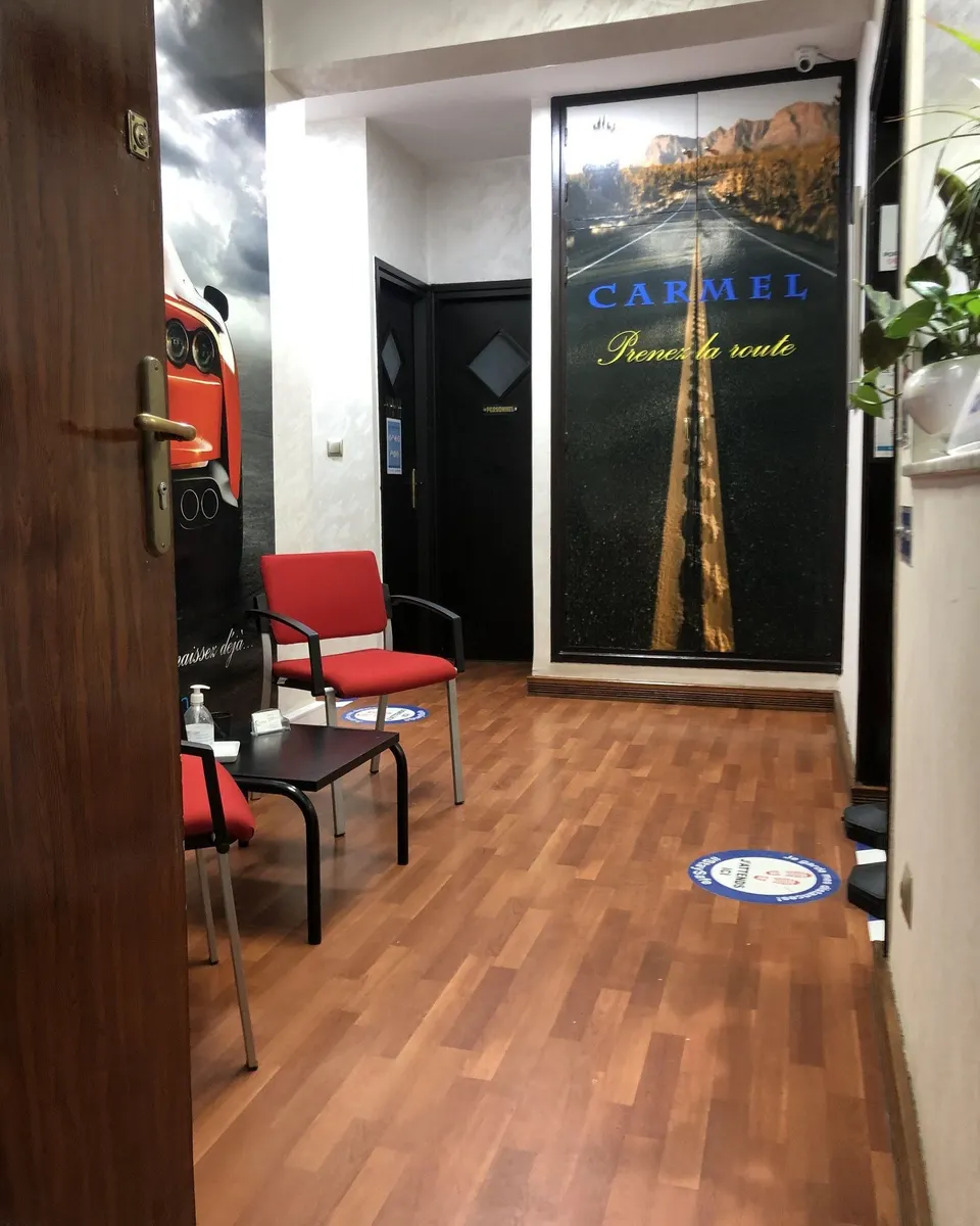 Couloir d’entrée de l’agence, porte vitrée décorée d’une route et du mot CARMEL