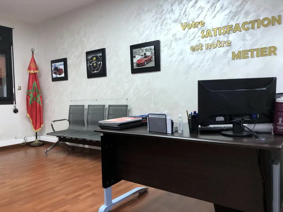 Accueil de l’agence, avec au mur « Votre satisfaction est notre métier » et des photos de voitures