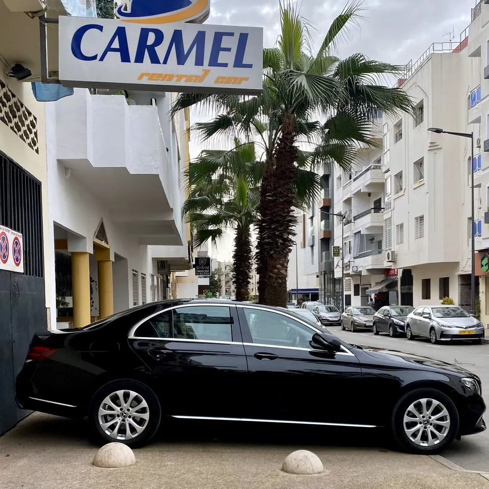 Mercedes Classe E noire garée sous l’enseigne CARMEL, rue Jabal Oukaïmeden à Agdal